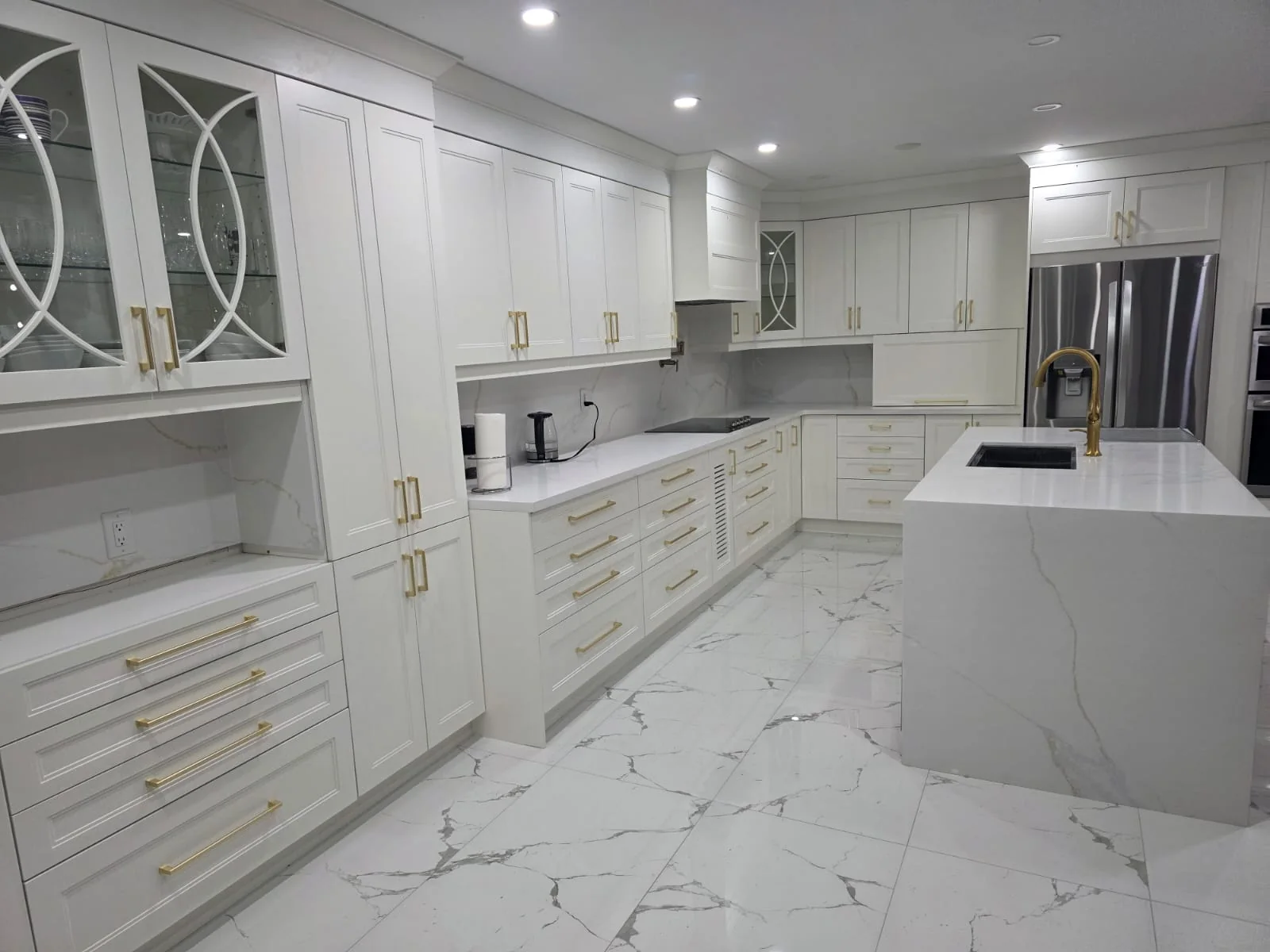 Completed white custom kitchen cabinets with brass hardware, stone surfaces and a large island